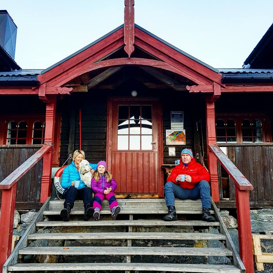 Familie med hund sitter på trappen utenfor Silsethytta og drikker kaffe